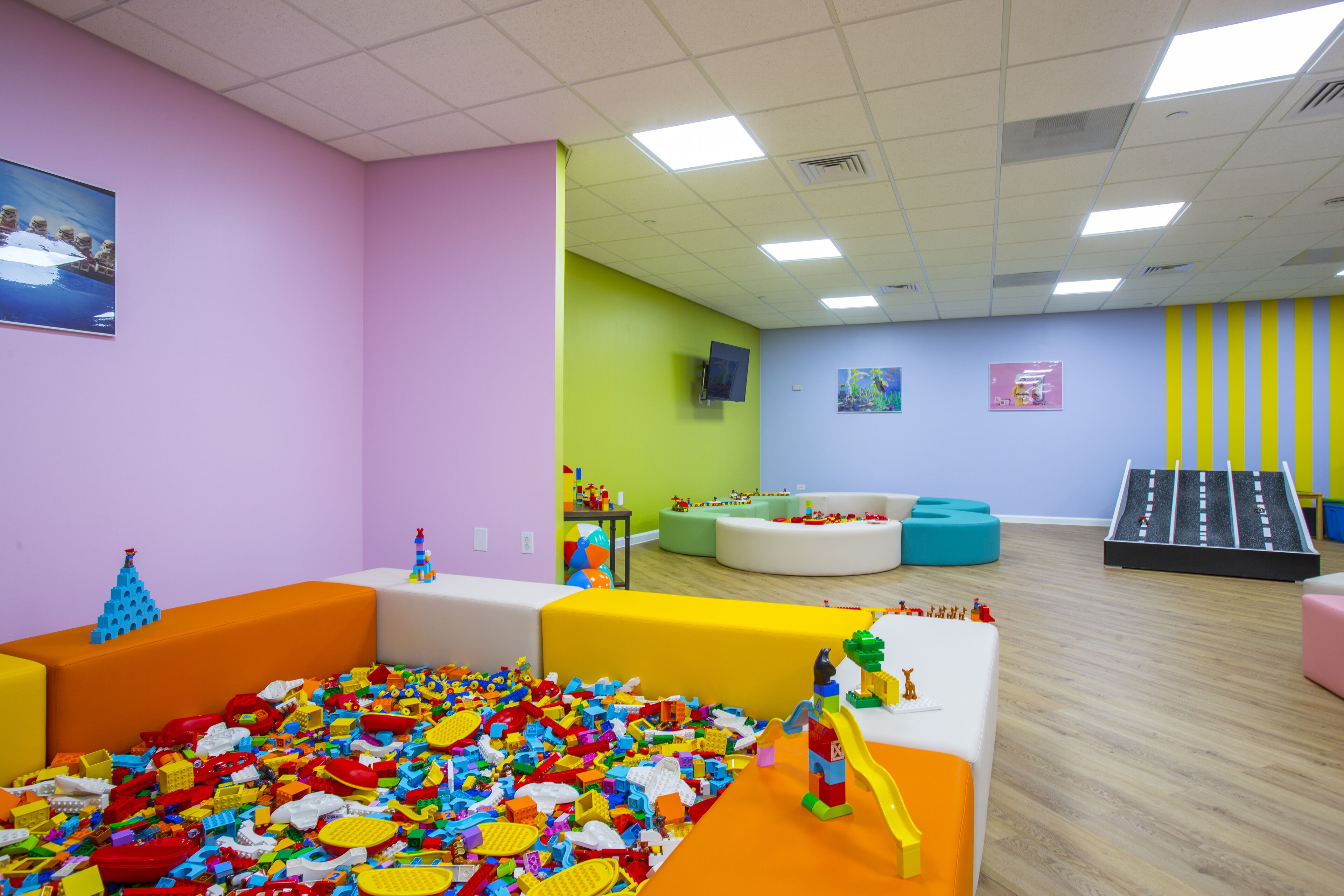 Una sala de juegos con paredes coloridas, una zona de juegos con juguetes y un tobogán.
