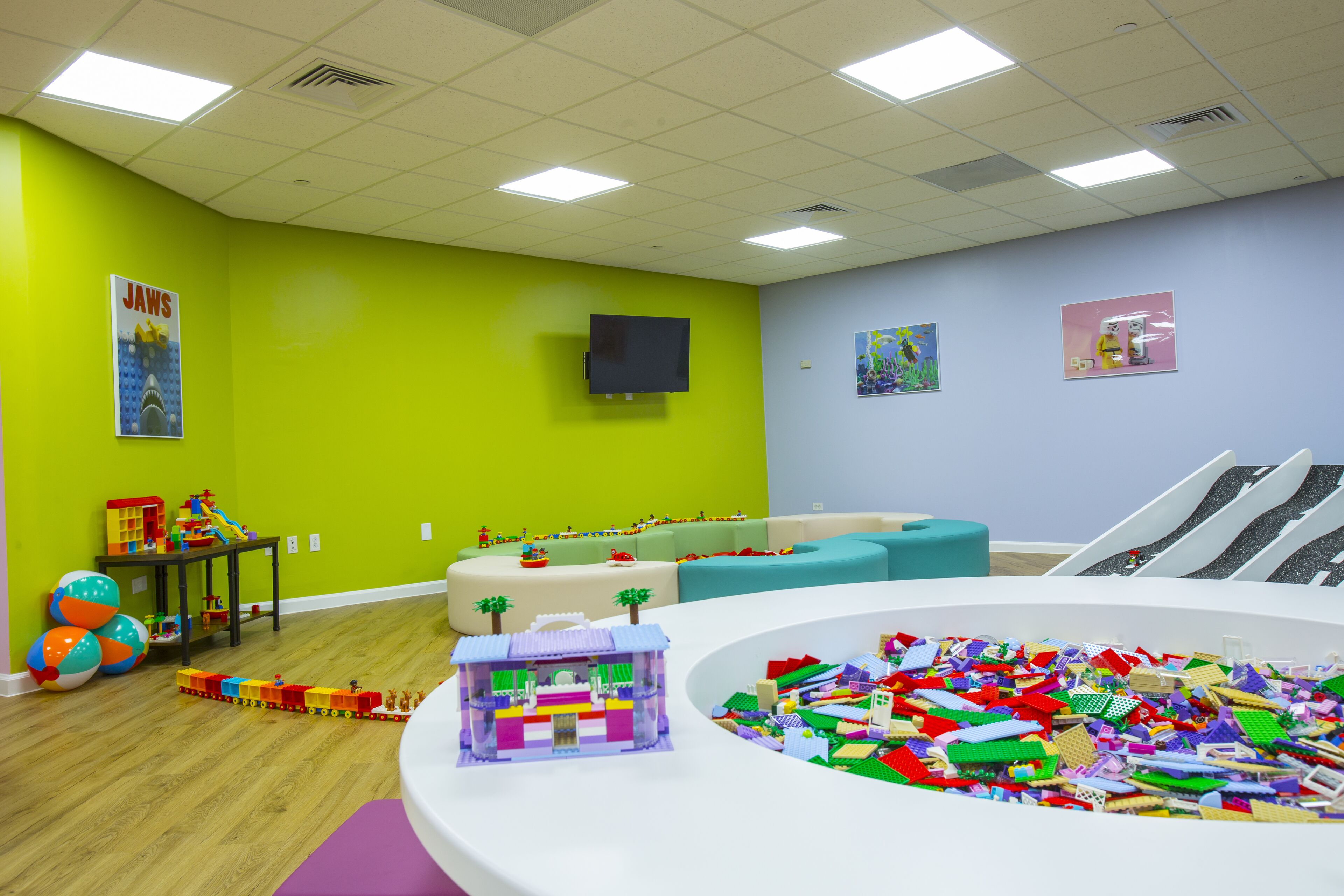A playroom with a train set, a large pile of building blocks, and a television mounted on the wall.