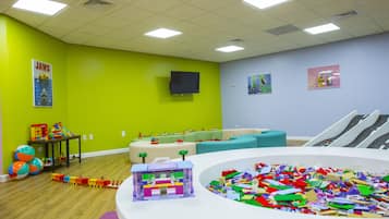 A playroom with a train set, a large pile of building blocks, and a television mounted on the wall.