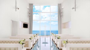 A church interior with pews, a glass table, and a view of the ocean through large windows.