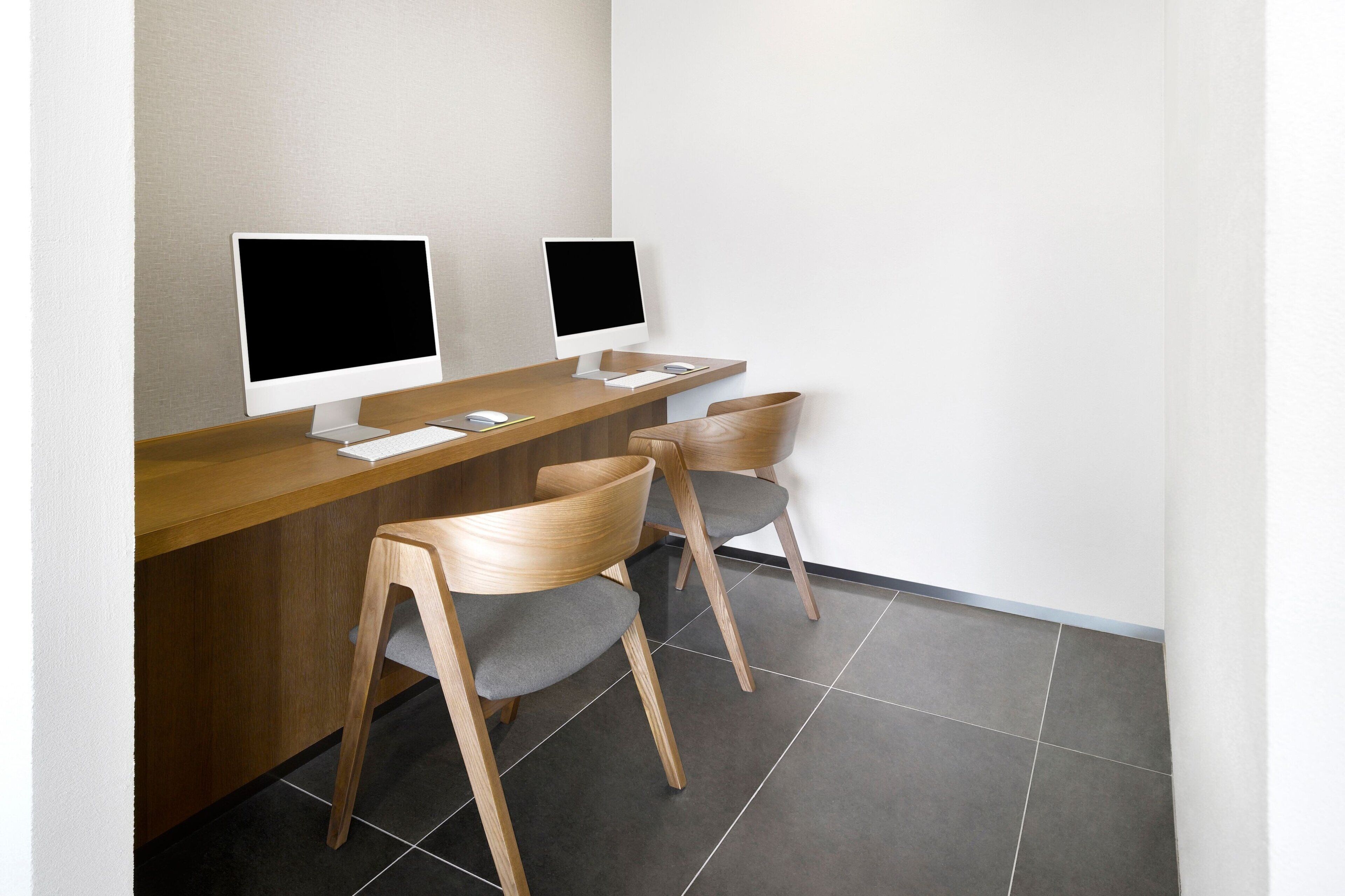 Un espacio de trabajo moderno con dos computadoras de escritorio, un escritorio de madera y dos sillas.