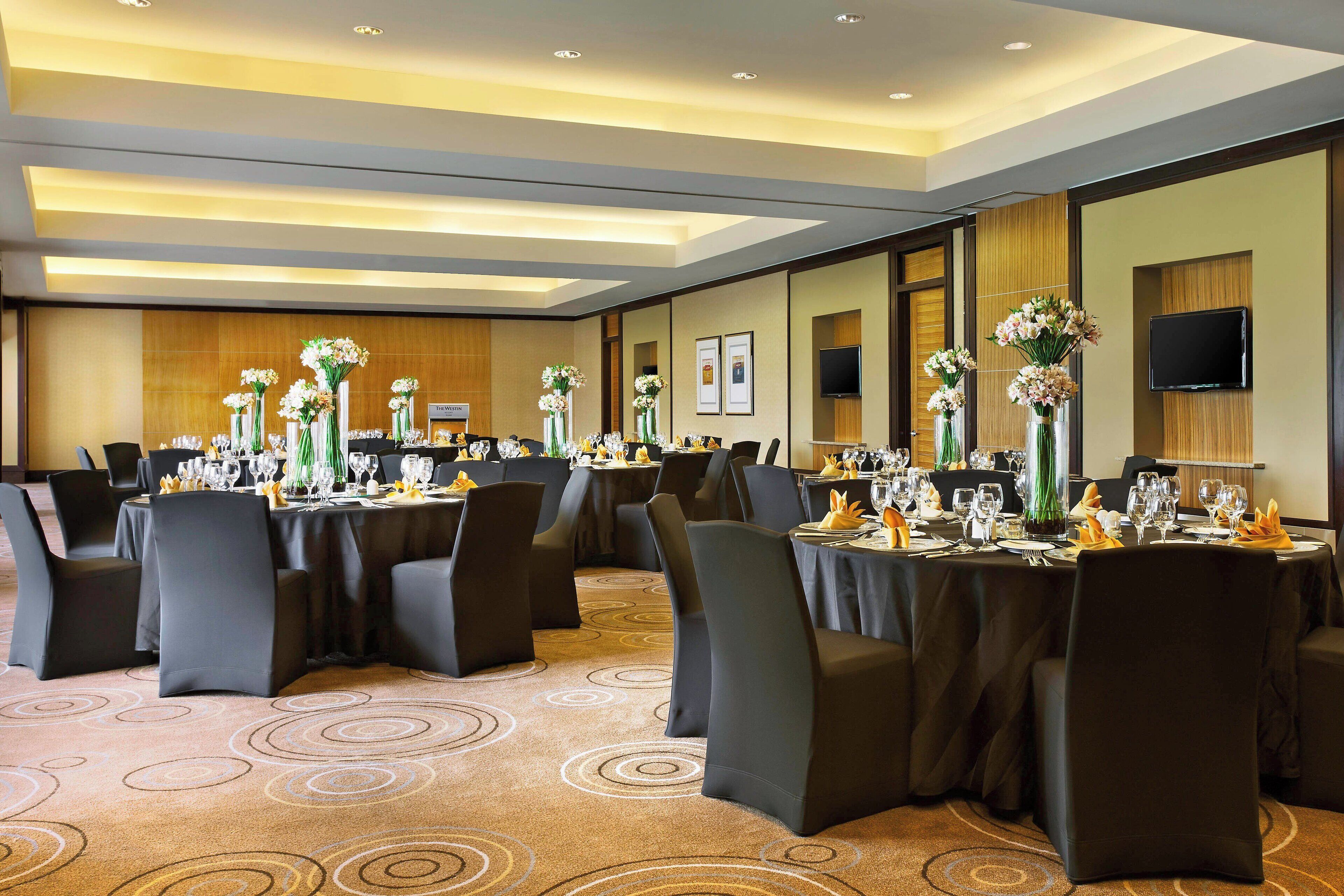 A conference room with round tables, black chairs, and floral centerpieces.