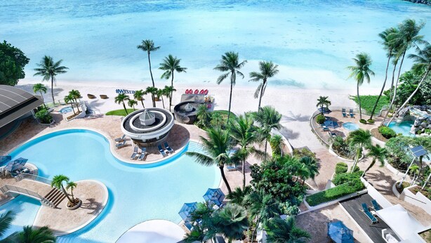 A resort with a swimming pool, beach, and palm trees.