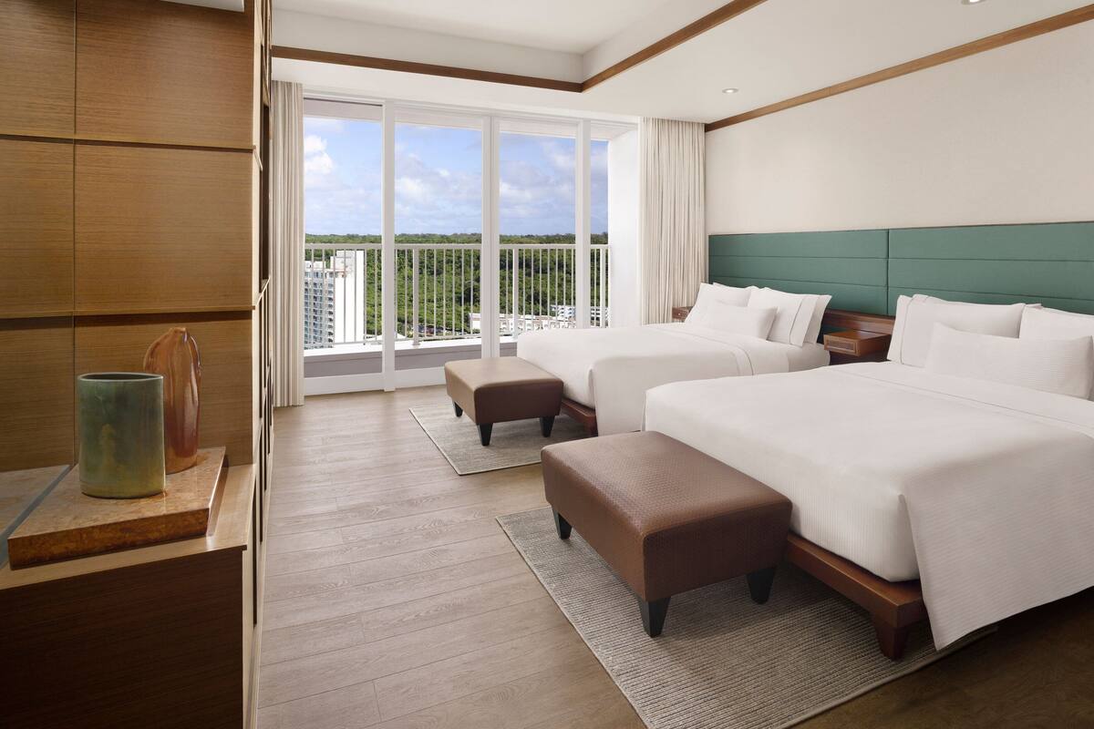 A hotel room with two beds, a large balcony with a view, and a wooden floor.