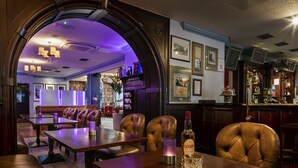 A restaurant with wooden tables and leather chairs, a bar area with a menu, and framed pictures on the wall.