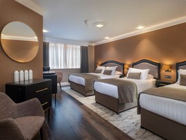 Habitación de hotel con dos camas, un escritorio, una silla, un espejo redondo y una ventana con cortinas.