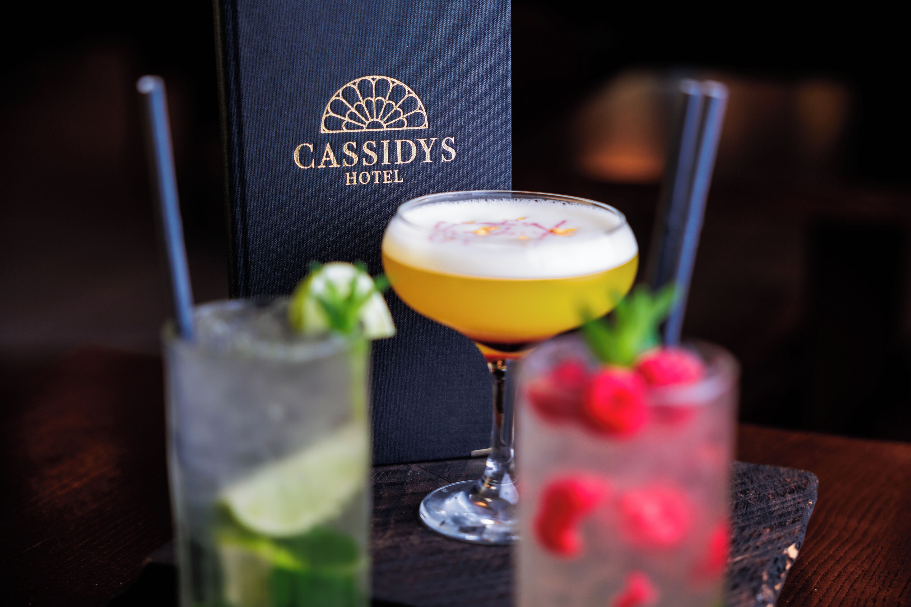 Three cocktails on a table with a black box labeled "Cassidy's Hotel" in the background.