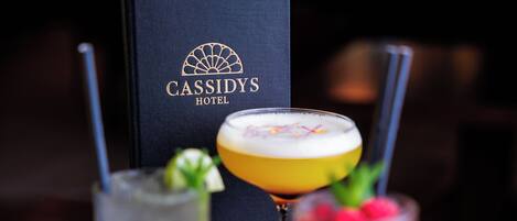 Three cocktails on a table with a black box labeled "Cassidy's Hotel" in the background.