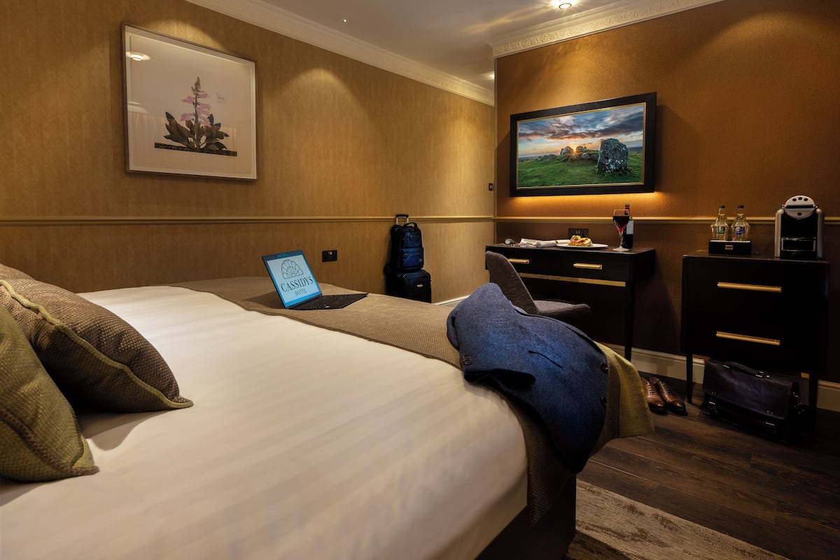 Habitación de hotel con cama, escritorio con una laptop, un cuadro y una lámpara de escritorio.