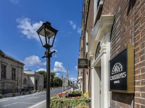 A street view with a hotel sign, a lamp post, and a building with a clock tower in the background.