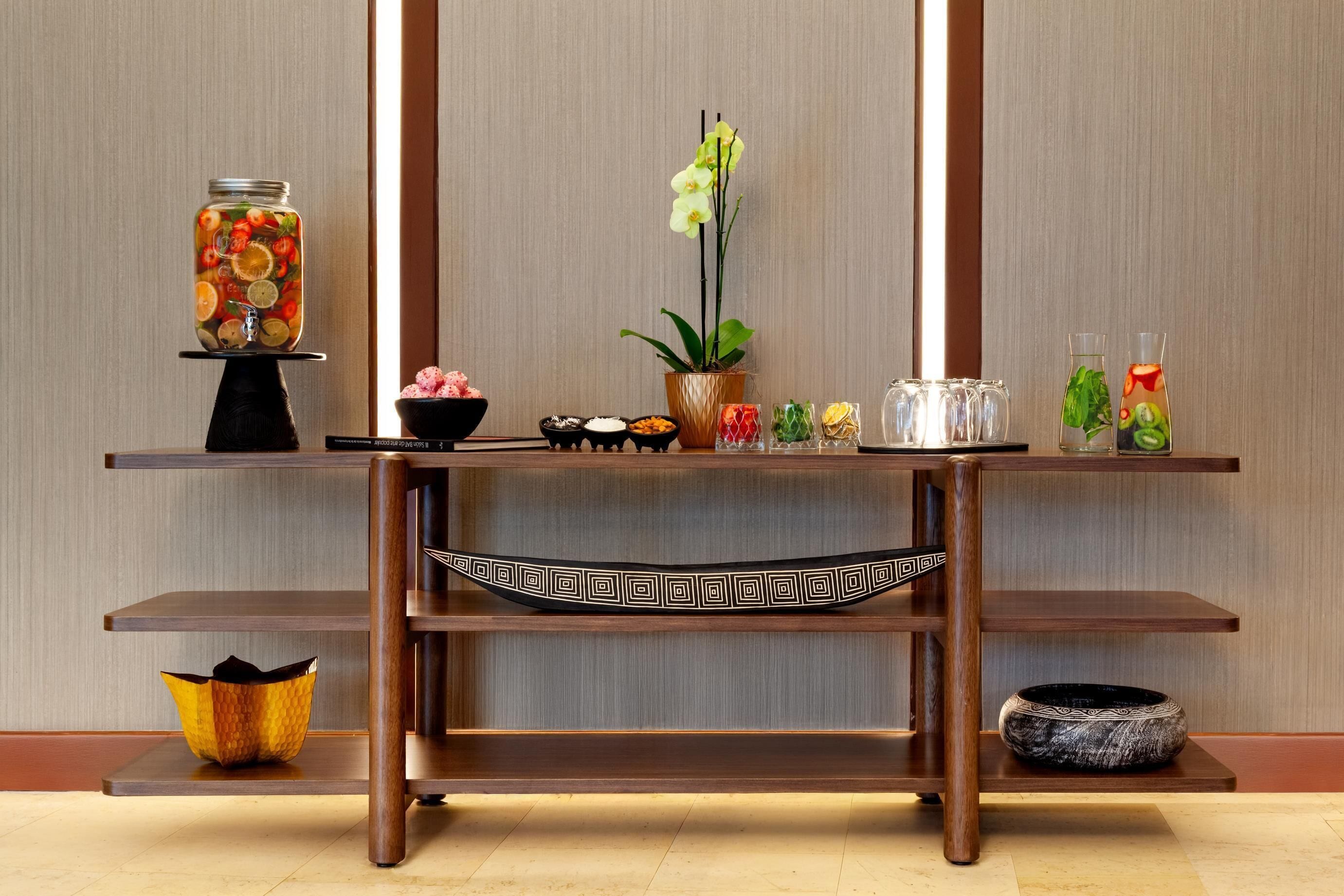 A wooden table with a decorative bowl, a potted orchid, and a jar of preserved fruits.