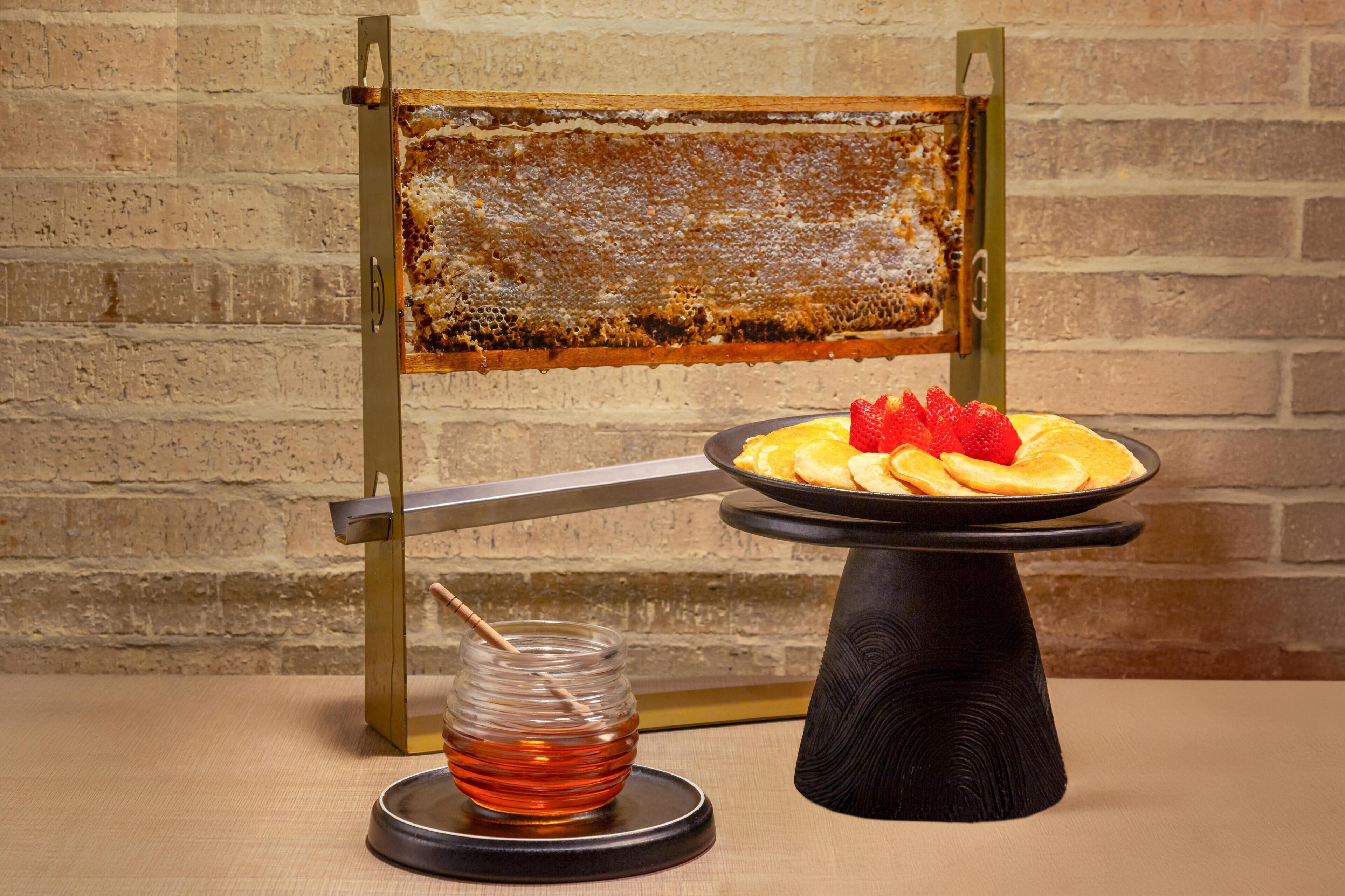 A honeycomb frame, a plate with pastries and strawberries, and a jar of honey on a table.