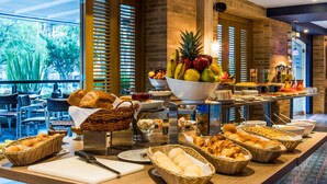 Un buffet proposant une variété de fruits, de viennoiseries et de pains, avec vue sur l’extérieur.