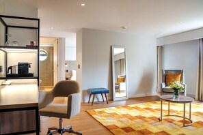 Een moderne woonkamer met een houten vloer, een ronde salontafel, een blauwe poef, een grijze fauteuil en een grote spiegel.