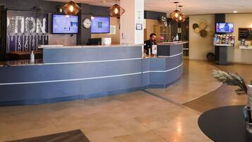 Un espace d’accueil avec un comptoir bleu incurvé, deux écrans d’ordinateur, une horloge et un téléviseur fixé au mur.