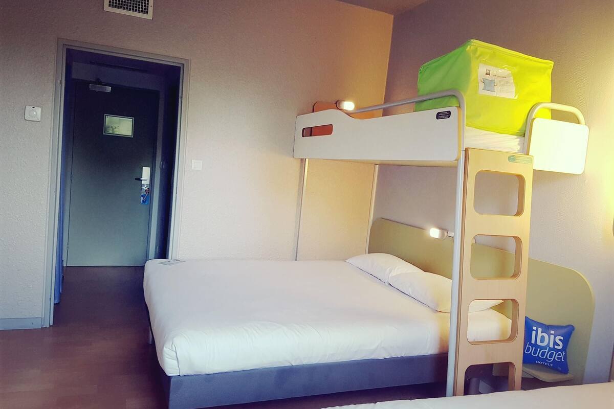 A bunk bed room with a door, a light fixture, and a pillow with 'ibis budget hotels' text.