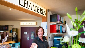 A reception desk with a sign reading "CHAMBRES" and "Salle Corot". There are bookshelves with binders and a computer monitor on the desk.