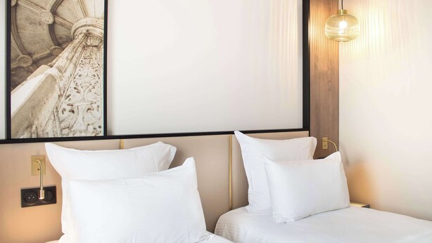 A hotel room with two beds, a large framed picture on the wall, a wooden headboard, and a hanging light fixture.
