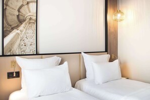 Habitació d'hotel amb dos llits, un quadre gran amb marc a la paret, un panell de fusta al capçal i un llum penjant.