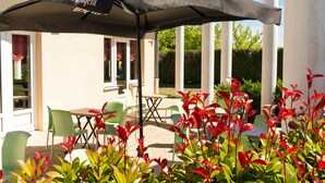 An outdoor patio with a table and chairs, a black umbrella, and red plants.