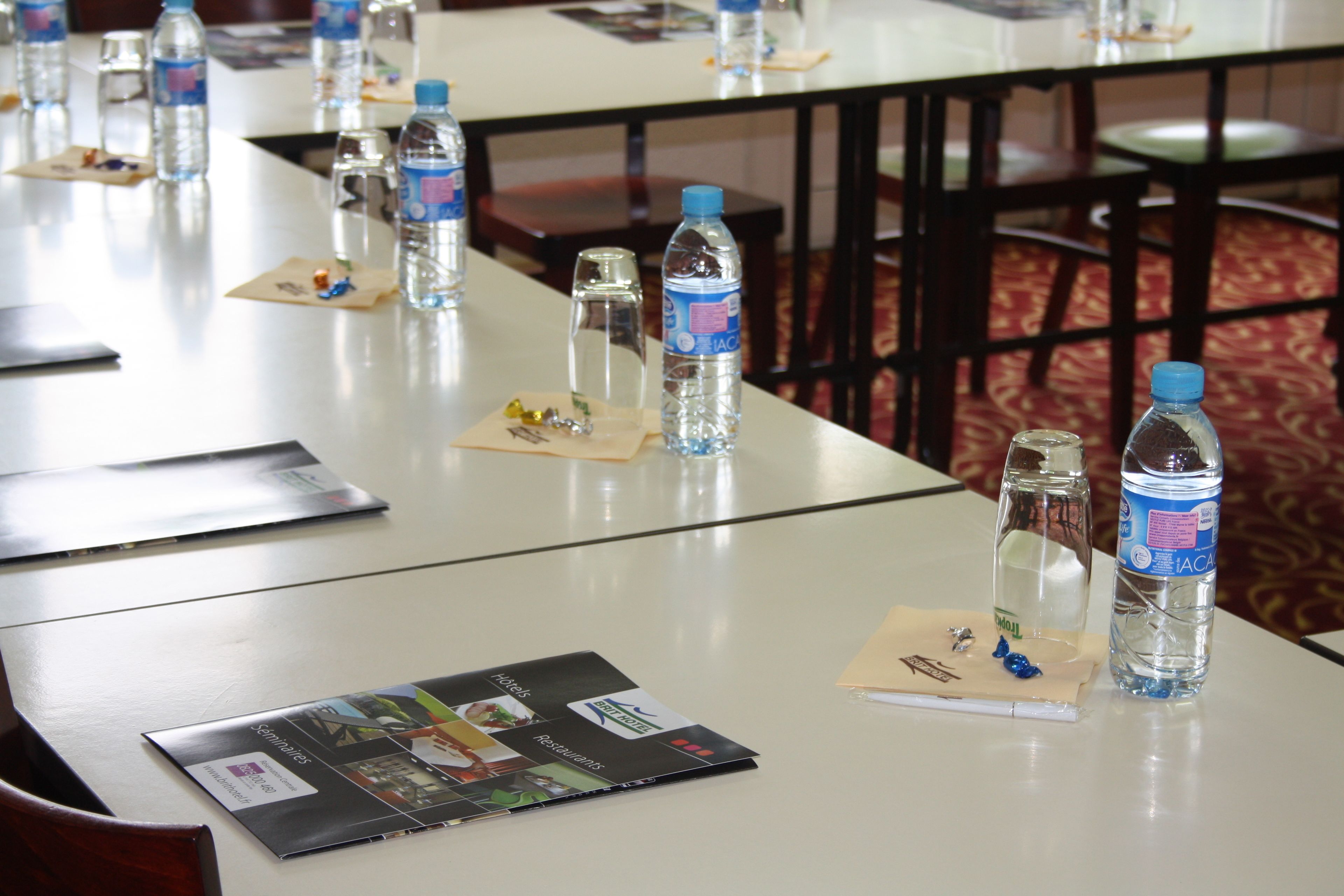 A conference room with tables set up for a meeting, each with water bottles, name tags, and brochures.