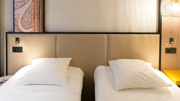 Two single beds with white linens and headboards, a wall-mounted artwork, and a modern light fixture.