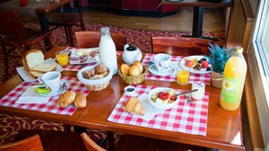 A breakfast table with bread, croissants, a fruit bowl, juice, and a bottle of orange juice.