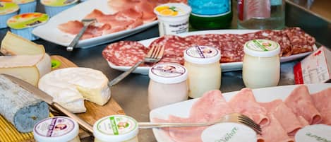 A variety of cheeses, cured meats, and jars of preserves on a table.