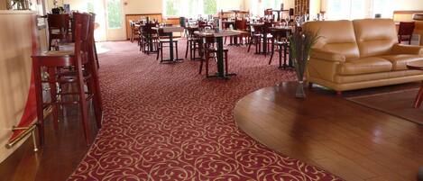 A spacious dining area with multiple tables and chairs, a central sofa, and a patterned carpet.