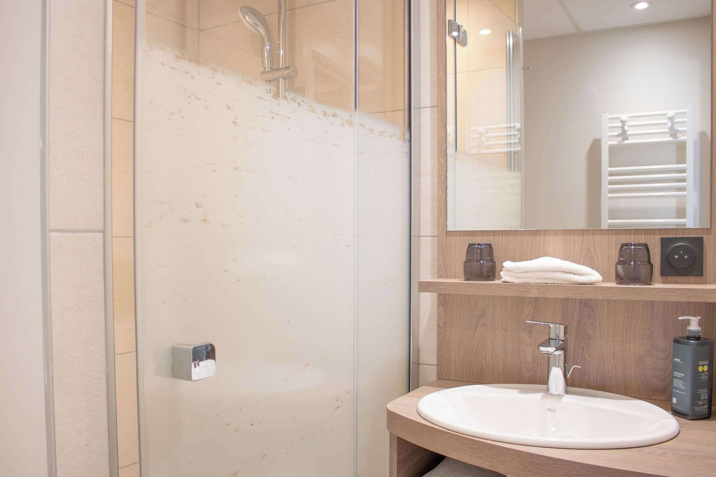A modern bathroom with a glass shower enclosure, a white sink, and a mirror above the sink.