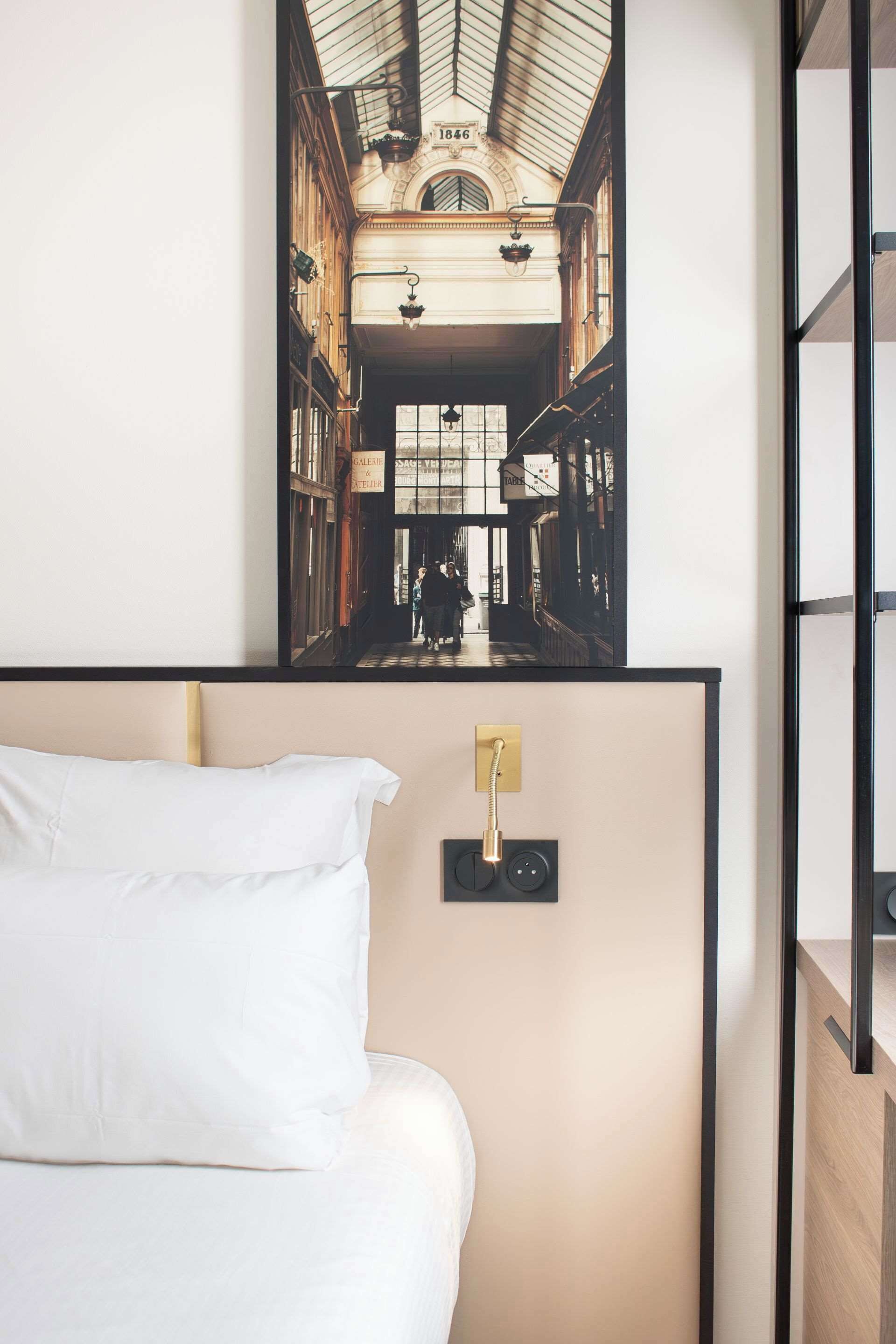 A hotel room with a bed, a wall-mounted light fixture, and a framed picture of a street scene.
