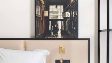A hotel room with a bed, a wall-mounted light fixture, and a framed picture of a street scene.