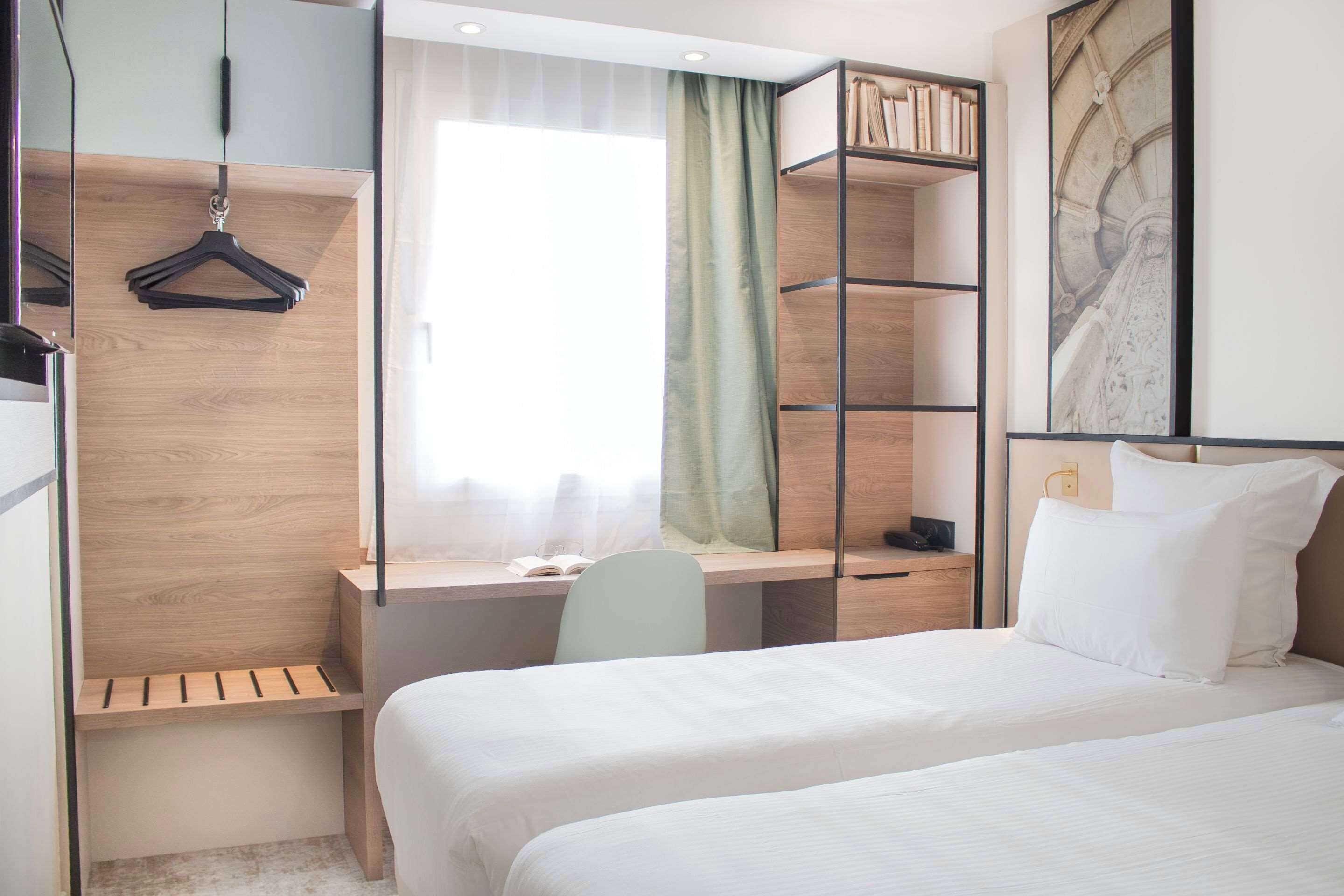A hotel room with a bed, a desk, a chair, a wardrobe, and a bookshelf.