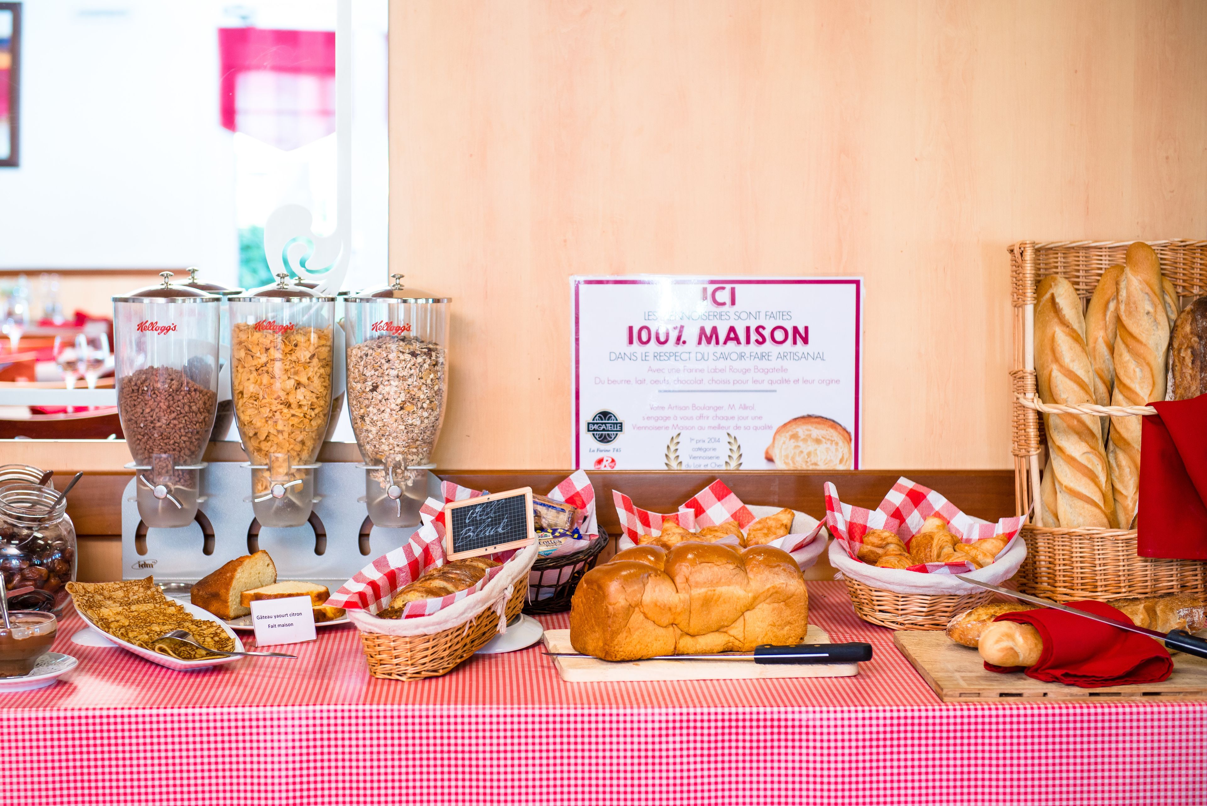 Un bufé de desayuno con diversos alimentos y un cartel que indica el compromiso de la panadería con la calidad artesanal.