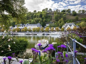 A riverside town with historic buildings, a dock with boats, and a bridge with purple flowers. - Mercure Namur Hotel (Namur)