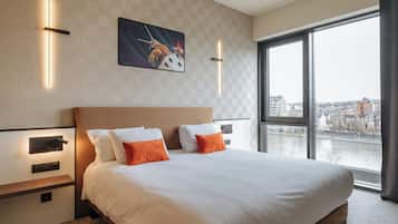 A hotel room with a large bed, two bedside tables, a nightstand, and a view of a river through large windows.
