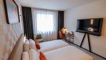 Habitación de hotel con dos camas, un escritorio con silla, un televisor de pantalla plana y un ventanal con cortinas.