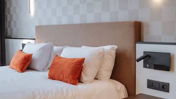 Une chambre d’hôtel moderne avec un grand lit, du linge de lit blanc, des oreillers orange, une tête de lit, une table de chevet, un panneau de commande fixé au mur et un tableau encadré accroché au mur.