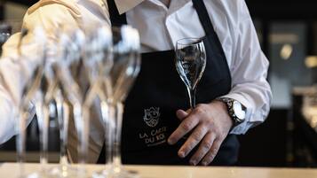Una persona sosteniendo una copa de vino con un logotipo en el delantal, de pie detrás de un mostrador con varias copas de vino.