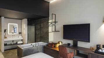 Ein modernes Hotelzimmer mit einem großen Bett, einem Schreibtisch, einem Flachbildfernseher, einem großen Spiegel, einer Badewanne und einer Dusche.