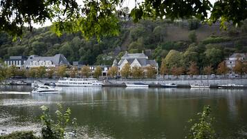 Une vue sur le fleuve, avec des bateaux, une colline parsemée d’arbres et des bâtiments le long de la rive.