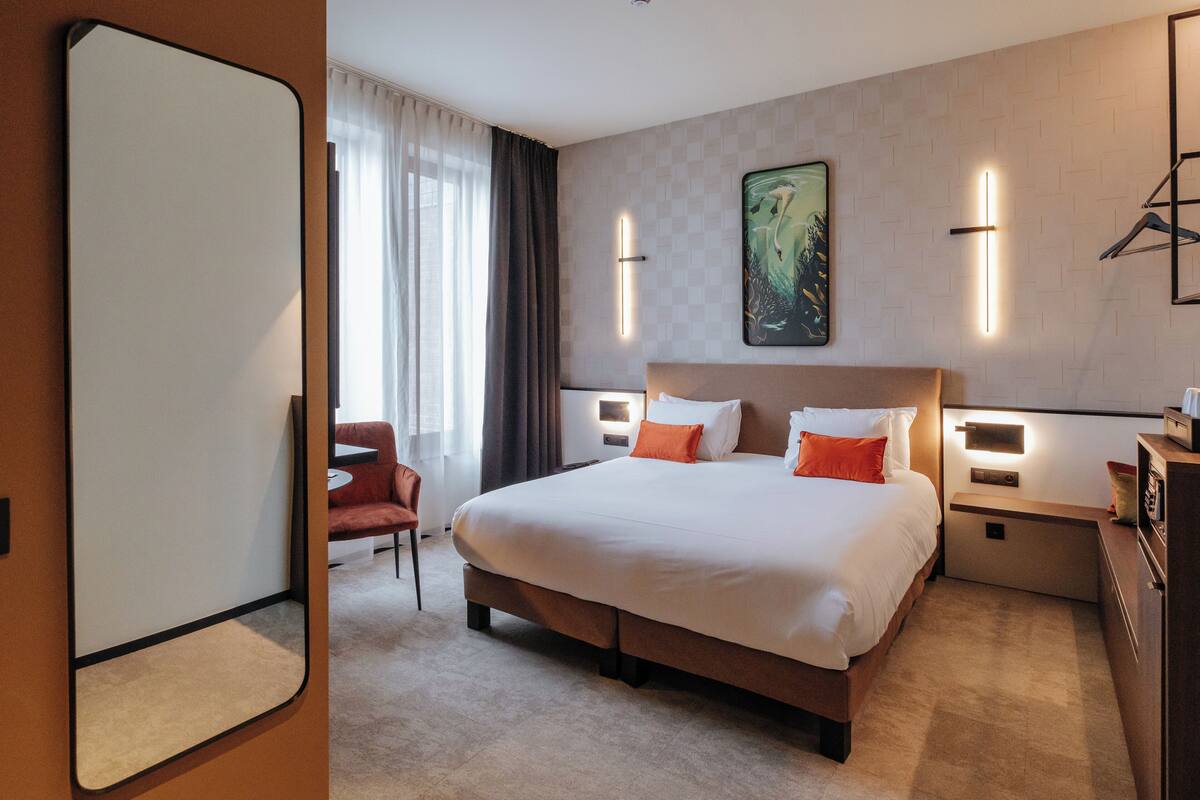 A hotel room with a large bed, bedside tables, a chair, and a painting on the wall.