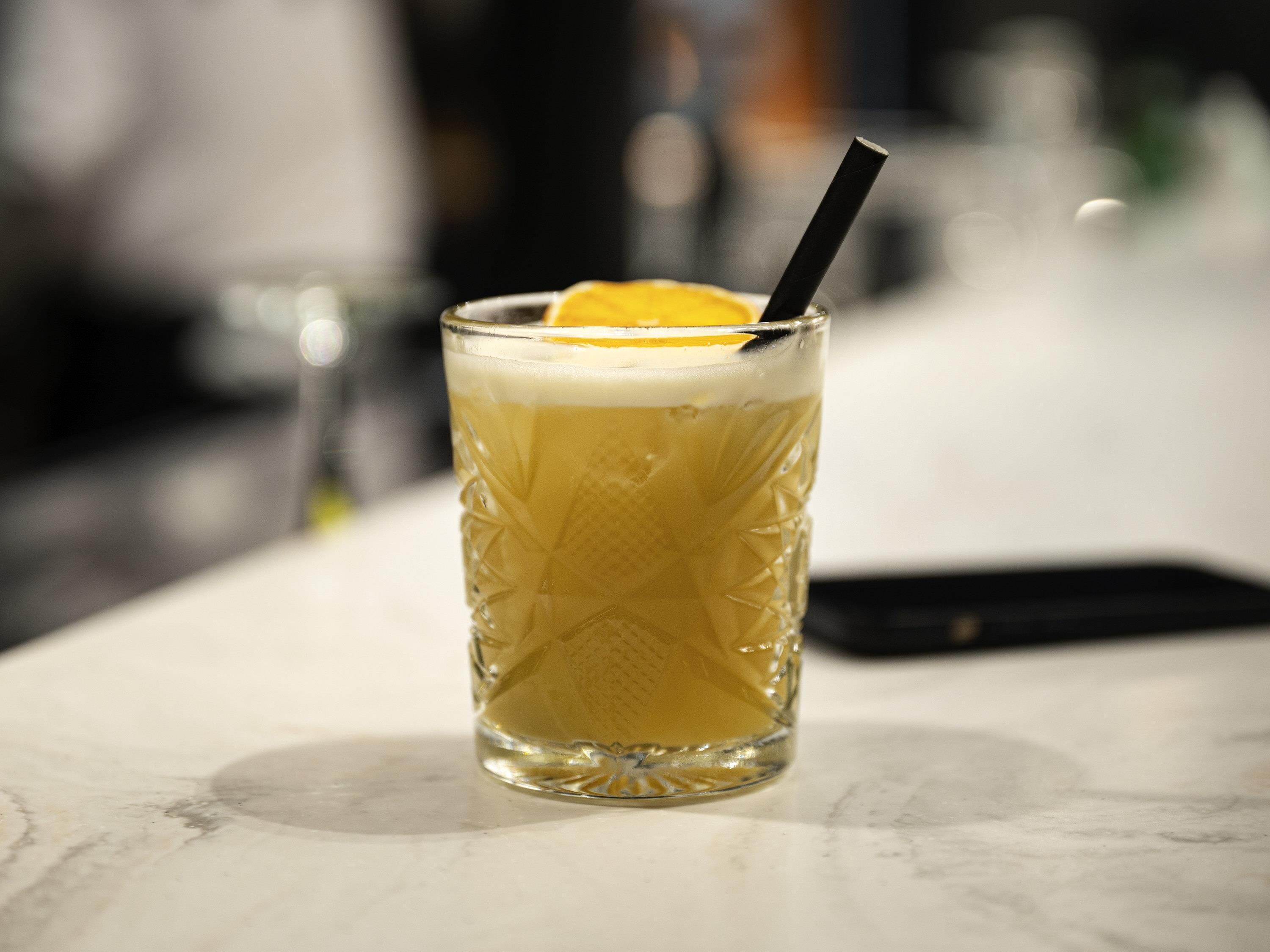 A glass with a straw and an orange slice on a marble surface.