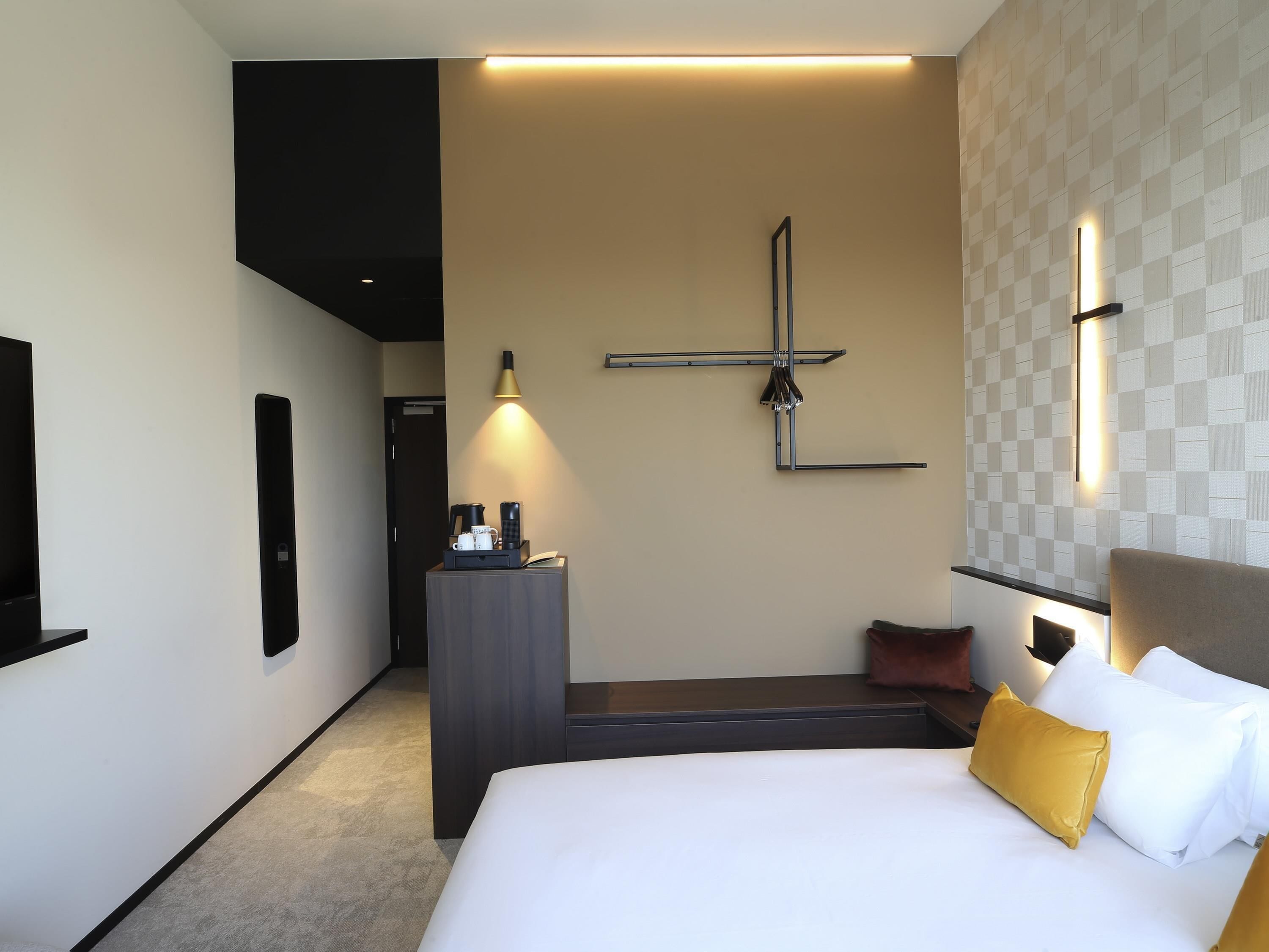 Une chambre d’hôtel équipée d’un lit, d’une table de chevet, d’un téléviseur fixé au mur et d’un luminaire moderne.
