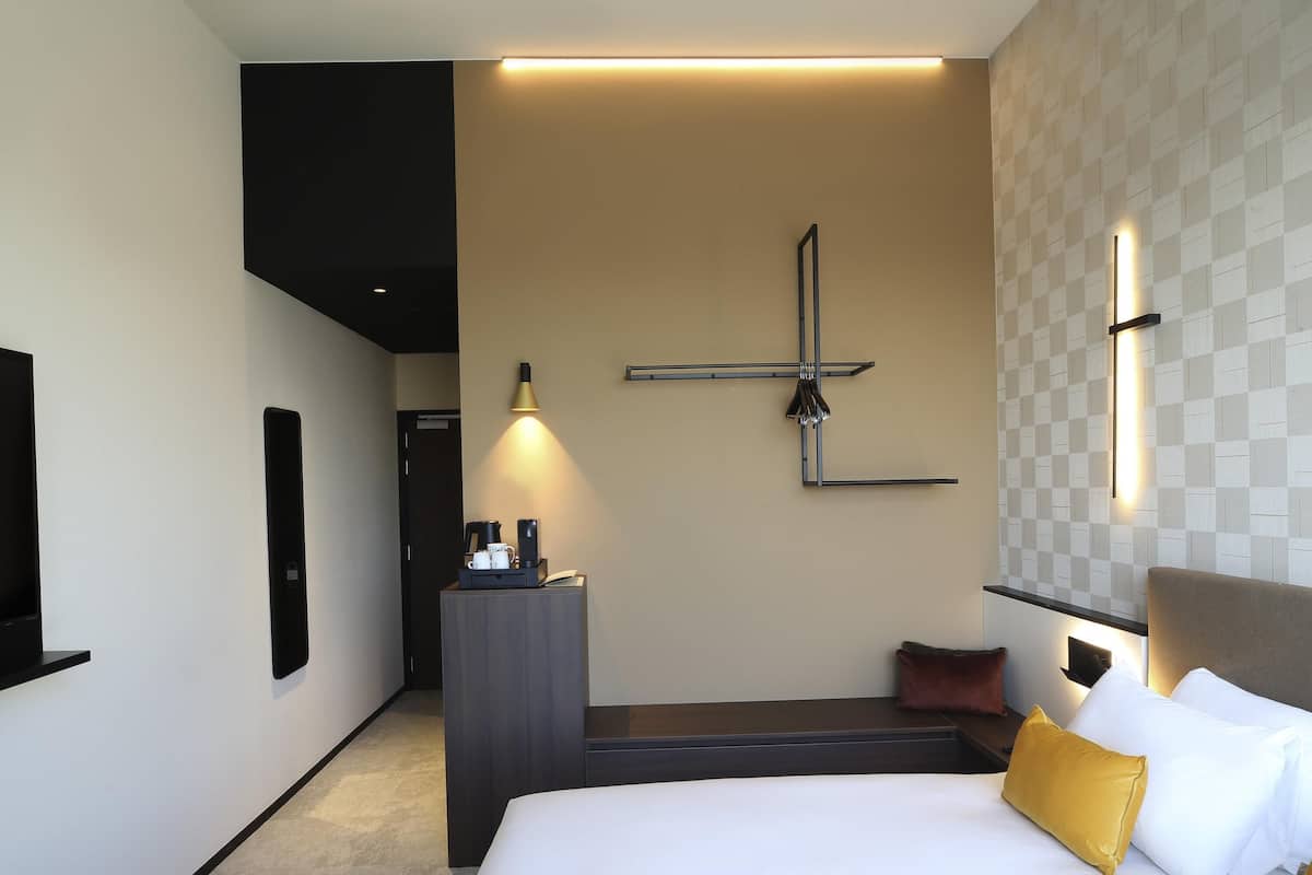 Une chambre dâhĂŽtel Ă©quipĂ©e dâun lit, dâune table de chevet, dâun tĂ©lĂ©viseur fixĂ© au mur et dâun luminaire moderne.