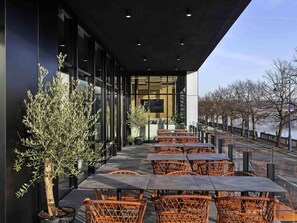 Un espacio al aire libre con mesas y sillas, un árbol en maceta y vistas a un río.