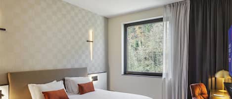 Habitación de hotel con una cama grande, un escritorio con silla, una ventana con vista a árboles y una pared con diseño geométrico.