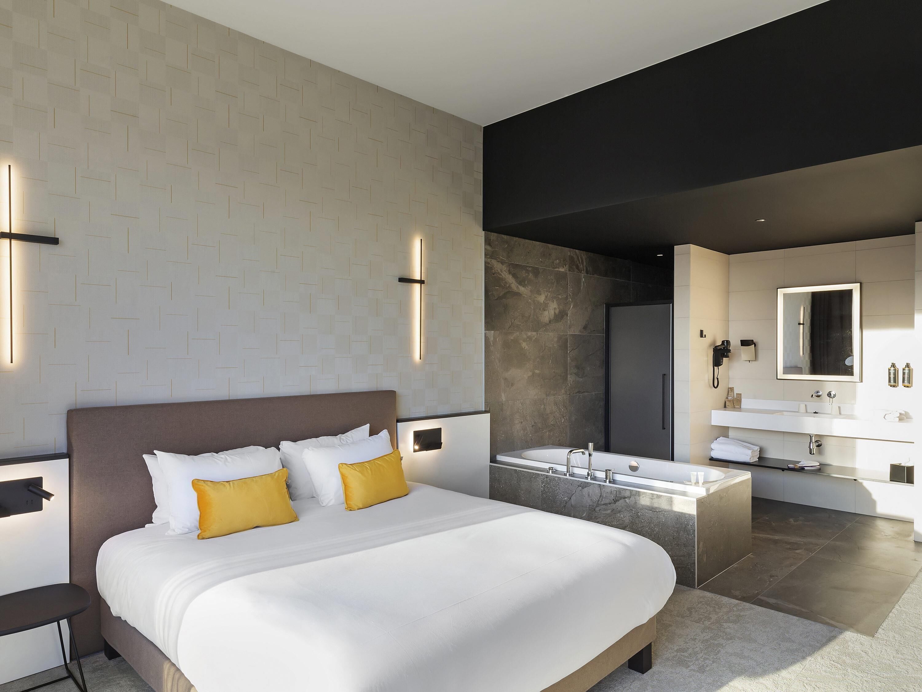 Een moderne hotelkamer met een groot bed, een badkamer met een badkuip en een wastafel met spiegel.