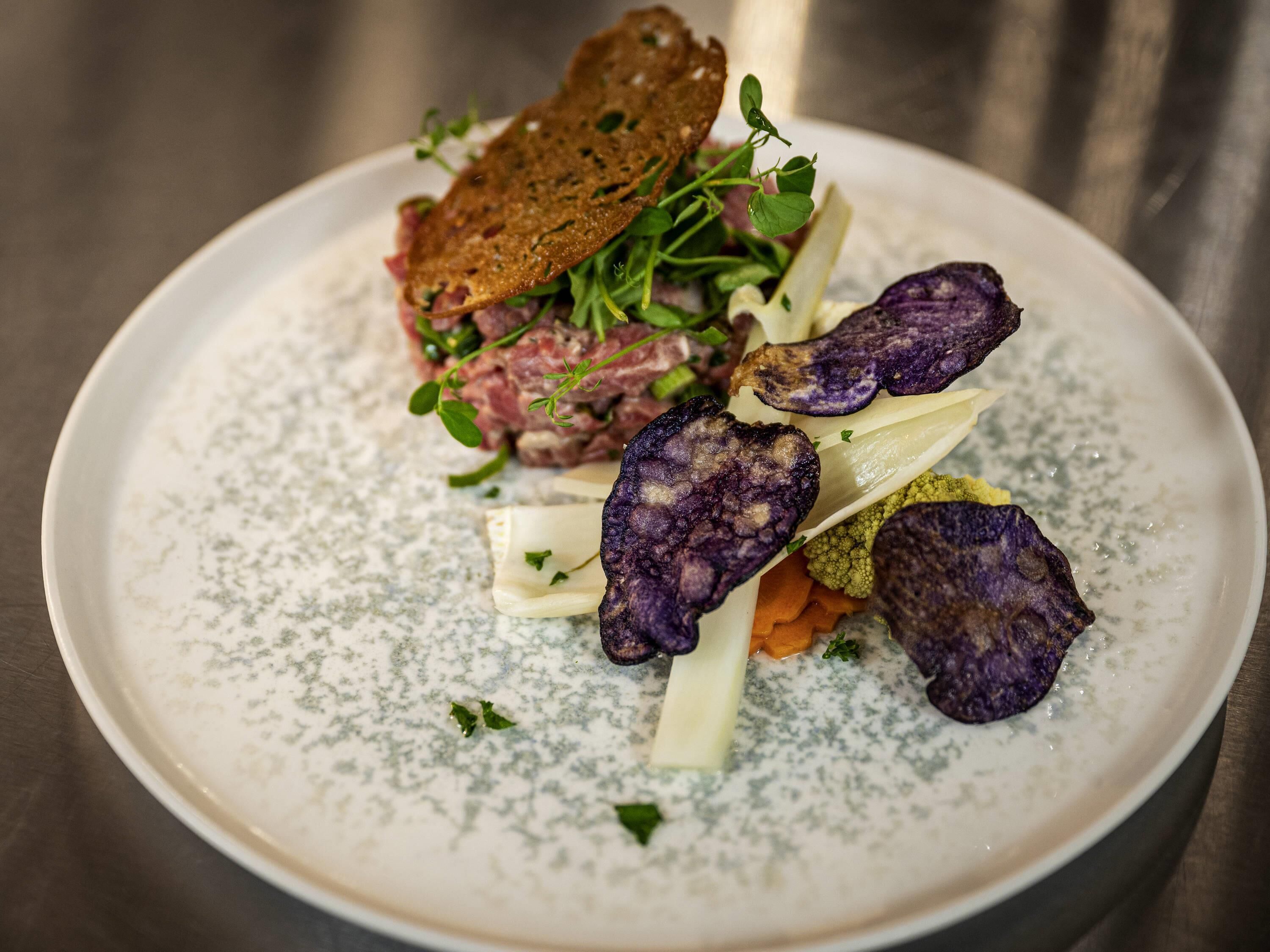 Ein Teller mit verschiedenen Speisen, darunter ein Stück Brot, ein Fleischgericht und violettes Gemüse.