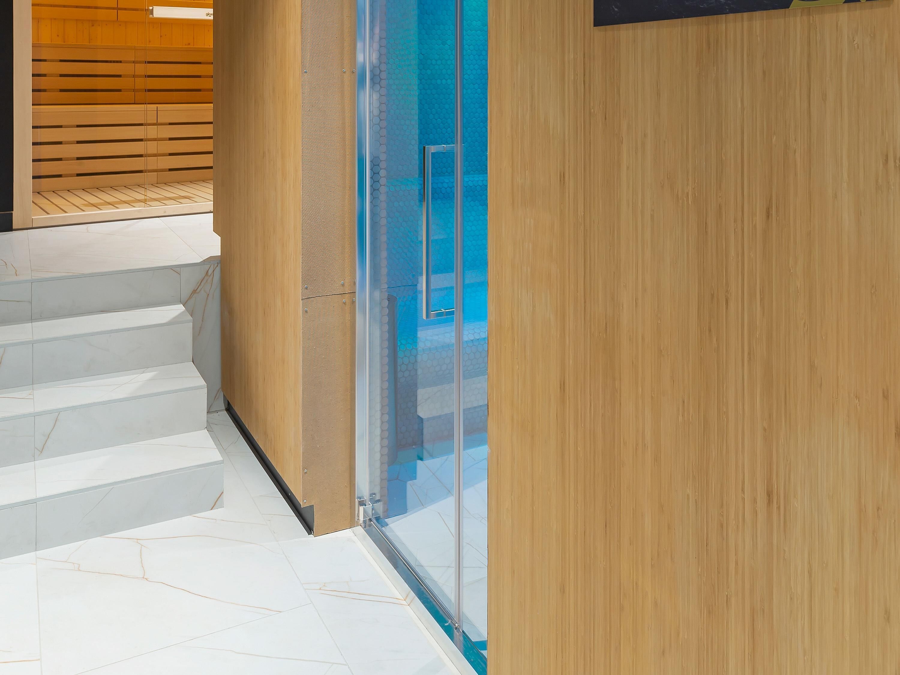 Un interior moderno con una escalera que baja a un nivel inferior, un separador de vidrio y una pared de madera.